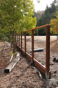 a wooden fence is in the middle of a dirt field with trees and logs around it