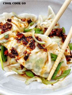 a white plate topped with dumplings covered in sauce and vegetables next to chopsticks