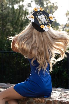 a woman sitting on top of a stone wall wearing a black hat with white flowers