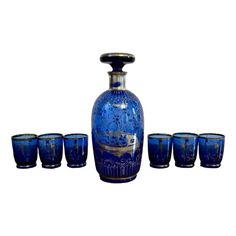 a blue glass vase with six glasses in front of it on a white background,