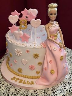 a barbie doll sitting on top of a cake with pink frosting and gold decorations