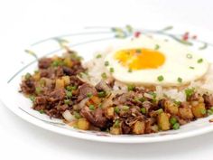 a white plate topped with rice and meat next to an egg on top of it