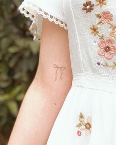 a woman with a small tattoo on her left arm, wearing a white dress and pink flowers