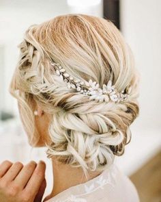 a woman with blonde hair wearing a braided updo and some flowers in her hair