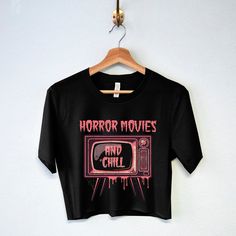 "\"HORROR MOVIES & CHILL\" Women's Halloween Crop Top Shirt Indulge in the thrills and chills of Halloween nights with our horror movie marathon t-shirt.  Shirt Colors: Black, Natural Shirt Sizes: S, M, L, XL, XXL Cotton Blend HORROR MOVIES & CHILL Crop Top Shirt, women's Halloween horror movies t-shirt, scary movie shirts, Halloween crop top tees, cropped tops" Black Graphic Print Crop Top For Halloween, Casual Halloween Graphic Print Crop Top, Horror-themed Short Sleeve Top With Screen Print, Horror Screen Print Short Sleeve Top, Horror Themed Short Sleeve Screen Print Top, Scary Movie Shirts, Halloween Crop Top, Cropped Outfits, Horror Movie T Shirts