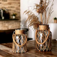 two vases sitting on top of a wooden table next to each other with dried plants in them