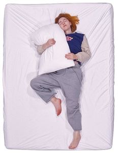 a woman laying in bed with a pillow on her back