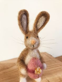 a needled bunny holding an apple on top of a wooden table next to a white wall