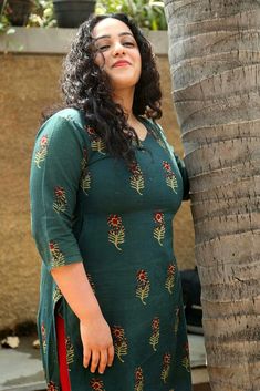 a woman standing next to a palm tree wearing a green dress with red flowers on it