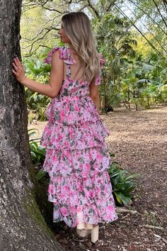 a woman standing next to a tree wearing a pink floral dress with ruffles