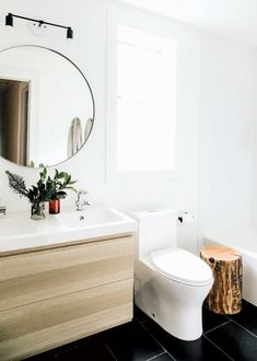 a white toilet sitting next to a bathroom sink under a round mirror on a wall