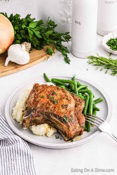 a white plate topped with meat and green beans next to garlic, parsley and an onion