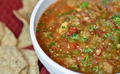 a white bowl filled with soup next to tortilla chips on a red cloth