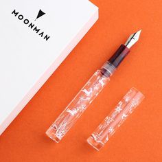 two pens sitting on top of an orange surface next to a box with the word woman written on it