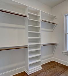 an empty walk in closet with white shelving and wood flooring on the side