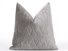 a gray pillow with pleated fabric on the front and back, sitting on a white surface