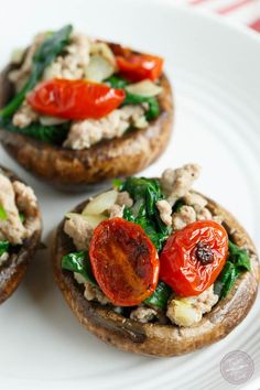 three open faced sandwiches with tomatoes, spinach and meat on them sitting on a white plate