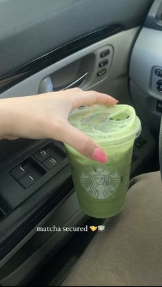 a person holding a starbucks cup in their hand next to a car dash board and steering wheel