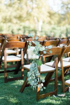 an outdoor ceremony with wooden chairs and greenery