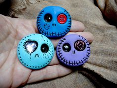 three buttons in the palm of someone's hand that have been decorated with skulls and hearts