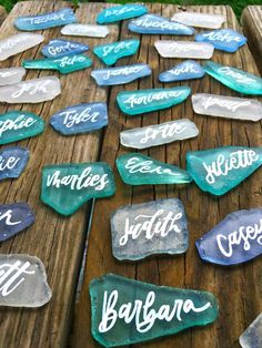 some glass rocks with names on them sitting on a wooden table in front of grass