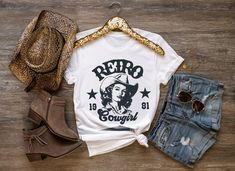 Step back in time with our Retro 80's Cowgirl Tee! This stylish t-shirt captures the essence of the 80's with a vibrant, vintage-inspired design featuring a bold cowgirl graphic.  Made from soft, high-quality cotton, it offers both comfort and durability, making it an ideal choice for everyday wear. Whether you're heading to a casual outing or a themed party, this retro tee is sure to make a statement and bring a nostalgic vibe to your wardrobe! * 100% combed and ring-spun cotton * Heather Prism Lilac & Heather Prism Natural are 99% combed and ring-spun cotton, 1% polyester * Athletic Heather is 90% combed and ring-spun cotton, 10% polyester * Other Heather colors are 52% combed and ring-spun cotton, 48% polyester * Fabric weight: 4.2 oz/y² (142 g/m²) * Relaxed fit * Pre-shrunk fabric * Si Cowgirl Graphic, 90s Era, Vintage Cowboy, Retro Tee, Cow Girl, The 80's, Step Back, Vintage Inspired Design, Back In Time