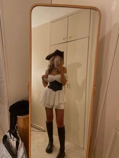 a woman taking a selfie in front of a mirror with her hat and boots