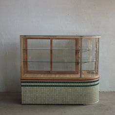 an old fashioned display case sitting on the floor in front of a white wall with green and brown tiles