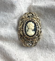 "You will receive this vintage cameo brooch from Gerry's. It measures 1 3/4\" x 1 1/8\" and is cast in an antiqued gold tone base metal. The cameo backing is black and the silhouette is a cream color. This brooch is in very good vintage condition with minimal signs of wear and a properly functioning safety catch. For finished vintage assemblage and vintage inspired necklaces, bracelets, and earrings, please visit us at our other Etsy store, William Dalton Design: www.williamdaltondesign.etsy.com Vintage Assemblage, Vintage Cameo, Cameo Brooch, One Ring, Native American Jewelry, Base Metal, Chain Pendants, Matching Earrings, Assemblage