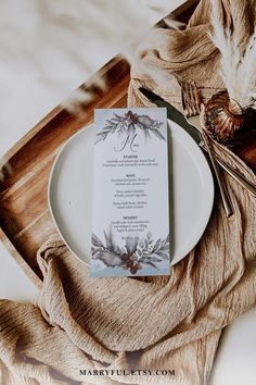 a place setting with a menu card and silverware on a wooden tray next to a feather