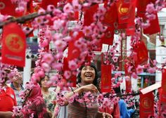 a woman standing under pink flowers in the middle of a street filled with red flags