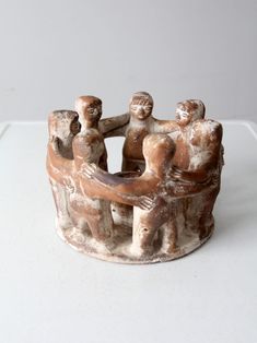 an old clay figurine with three people holding each other's hands on a white surface