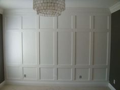 an empty room with white paneling and a chandelier