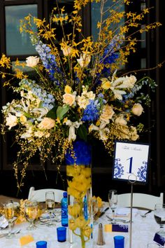 a vase filled with yellow and blue flowers sitting on top of a white table cloth