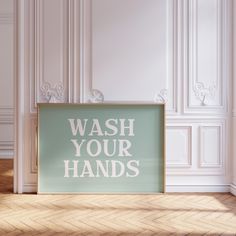 a sign that says wash your hands in white on a wooden floor next to a wall