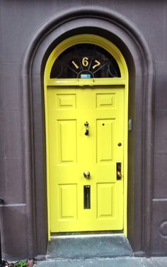 a yellow front door with a clock on it's face in the middle of an arch