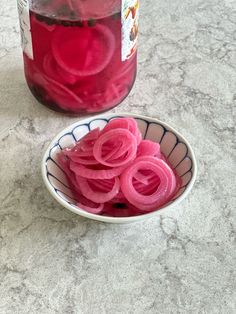 a bowl filled with sliced red onions next to a jar of pickled onion slices