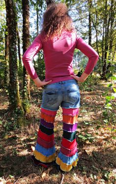 a woman standing in the woods with her back to the camera, wearing colorful pants