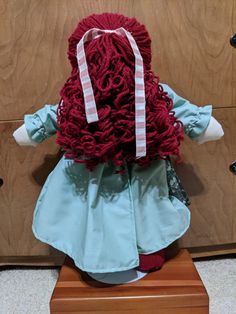 a doll with red hair is sitting on a wooden stand in front of a wall