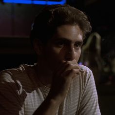 a man is sitting in the dark with his hand on his chin and looking at something