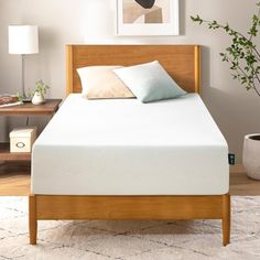 a bed with a wooden headboard and foot board in a white room next to a potted plant