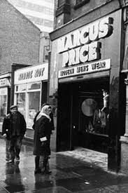 an old black and white photo of people walking in front of a store on a rainy day