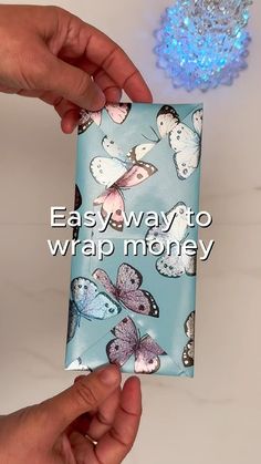 two hands are holding a blue gift bag with butterflies on it and the words easy way to wrap money