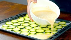 a person pours sauce over sliced cucumbers on a tray