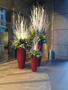 two red vases with white flowers and greenery are on the ground in front of a building