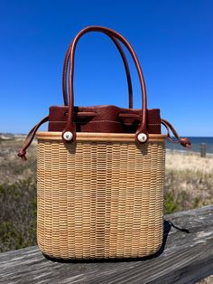 Handwoven Nantucket Lightship Basket Tote bag made by Abby Fisher. Tote features three sizes of staves in maple and cherry creating a stripe pattern on the front and back of the bag. The base and rim are made of maple and there are two Cherry inlays, one on the front of the rim and one along the top. The handles are 18” in leather to match the removable leather liner. The hydrangea charm is optional and can be purchased separately. Each piece has a logo button on the bottom of the bag with scrim Nantucket Basket, Nantucket Baskets, Basket Tote, 8 Weeks, Nantucket, Accessories Necklace, Basket Weaving, Stripes Pattern, Bag Making