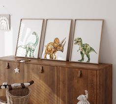 three framed dinosaurs are on top of a wooden cabinet