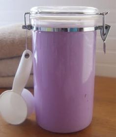 a purple container sitting on top of a wooden table next to a white spoon and towel