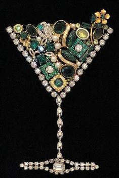 an elaborate green and gold brooch with jewels on it's side, in the shape of a triangle