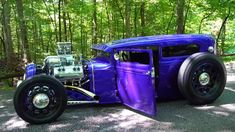 an old purple car is parked in the woods